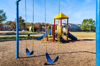 A playground with a yellow and red swing set and blue swings.